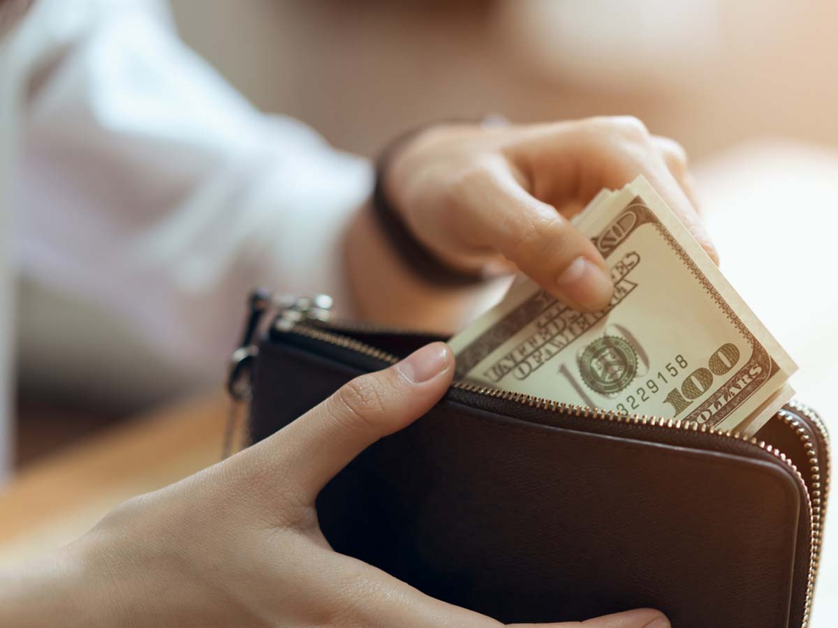 An image of a woman putting 100 dollar bills into her wallet.