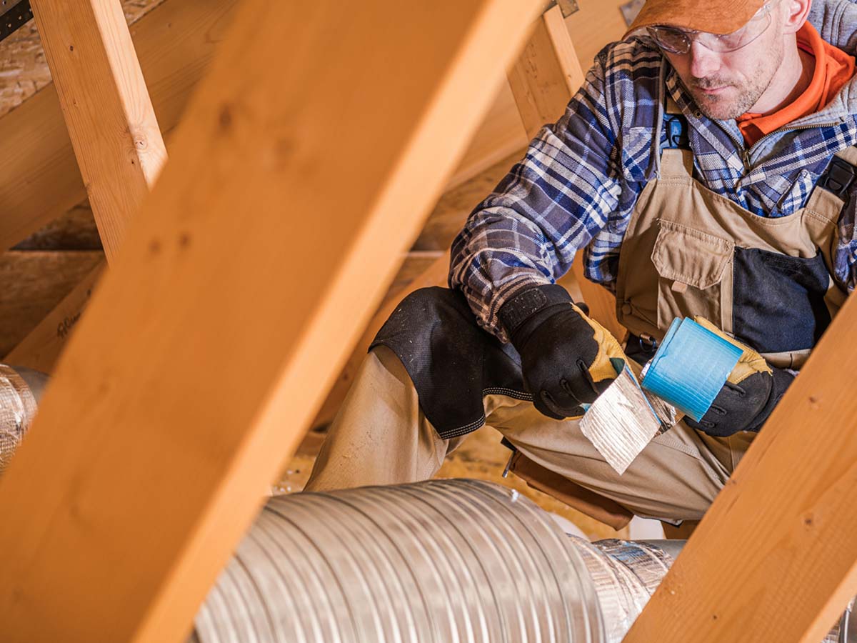 An image of a man fixing ductwork in the attic.